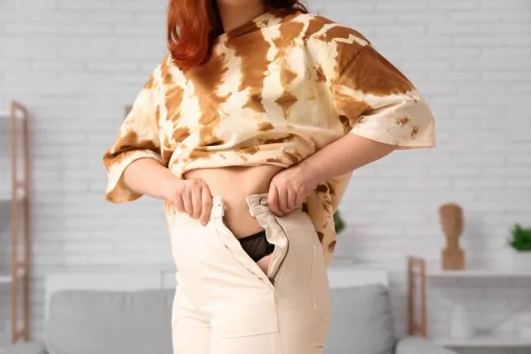 Image of woman trying to do her trousers up after pregnancy weight gain Hampton
