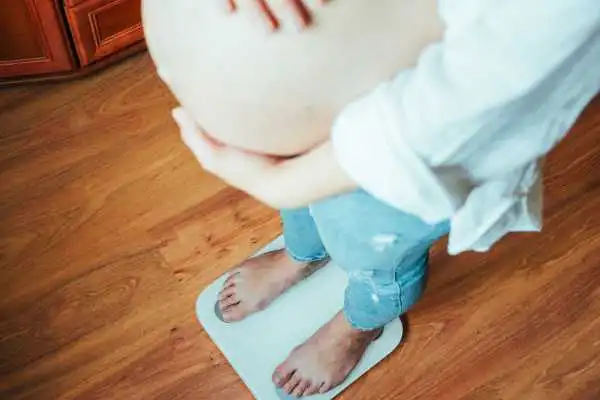 Image of woman weighing herself and experiencing weight gain through pregnancy Hampton